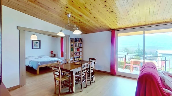 The open-plan living space at Casa-Isabelle is flooded with natural light and features a dining table with seating for six, perfect for enjoying meals together. The expansive windows offer breathtaking views of the surrounding mountains and valley, visib