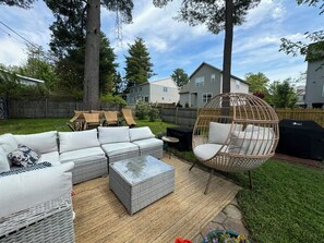 Backyard patio with outdoor couch, grill, lawn space and more.