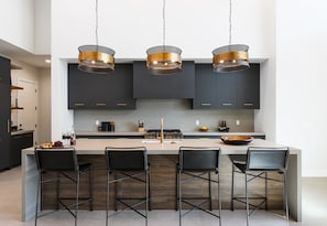 Unit 2: Fully equipped kitchen boasting high-end stainless steel appliances and a large island offering bar seating overlooking the formal dining area.