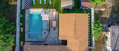 Aerial view showcasing the heated pool, life-size chess, bean bags, fire pit under a gazebo, outdoor dining, BBQ grill, pool loungers, and volleyball and basketball games—all designed for endless outdoor enjoyment.
