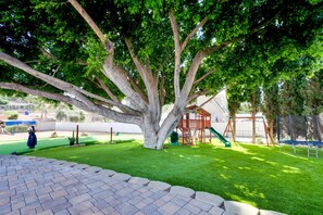 This expansive backyard offers endless fun for the whole family. A large, shady tree provides a natural playground, while the artificial turf makes for easy maintenance and year-round enjoyment. Kids can climb, slide, and swing on the playset, or practice