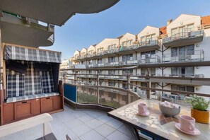  A view of a large balcony with a seating area, overlooking neighboring buildings and rooftops. The balcony is decorated with potted plants, creating a relaxing outdoor space.