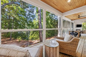 Expansive wrap-around screened porch with multiple seating areas and peaceful wooden lagoon view with glimpses of the golf course
