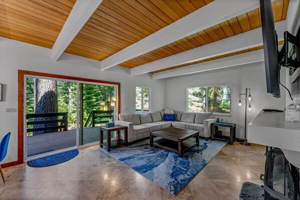 Living Room: L-shaped couch, wood burning fireplace, 50” Smart TV, access to deck and backyard