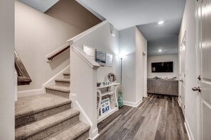 Welcoming entrance hallway with sleek vinyl plank flooring, stairs leading to the second floor on the left, and a glimpse of the inviting main floor living area ahead.