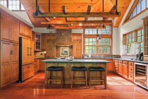 Spacious and fully equipped kitchen featuring rich wood cabinetry, a large center island with seating, and high-end appliances. With its beautiful wood-beam ceiling and ample natural light, this kitchen is perfect for cooking and entertaining.
