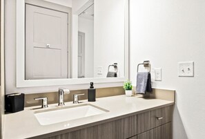 This bright and welcoming bathroom invites you to freshen up in comfort. Enjoy the forest-inspired shower curtain that adds a calming touch to your routine, complemented by the cozy rug underfoot and sparkling clean fixtures.