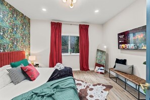 Unwind in this luxurious bedroom featuring a plush king bed, vibrant decor, and elegant red curtains. Enjoy streaming your favorite shows on the large TV and relax in the stylish, comfortable ambiance.
