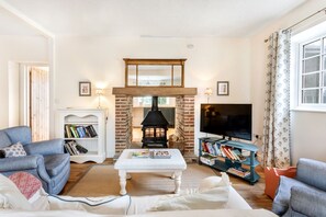 Relax by the two-way log burner in the cosy living room at Moat Cottage, with comfy seating and a dining table, connecting to the kitchen.