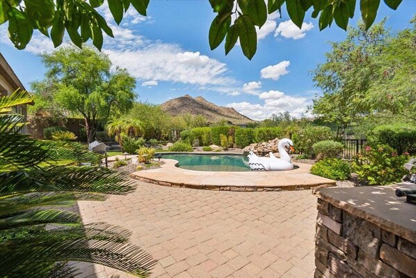 Beautiful backyard with a covered patio, sparkling pool, shaded seating, dining area, grill, and grass area.