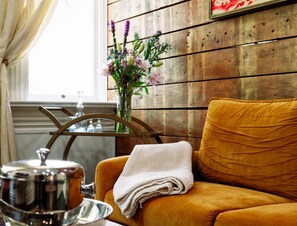 Comfy velvet sofa and throw with bar cart in the living room. Gorgeous distressed  painted wall treatment on original exposed shiplap.
