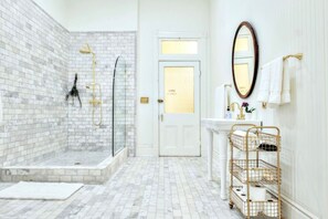 Enormous marble clad bathroom with oversized shower, brass fittings, console sink, and vintage mirror.