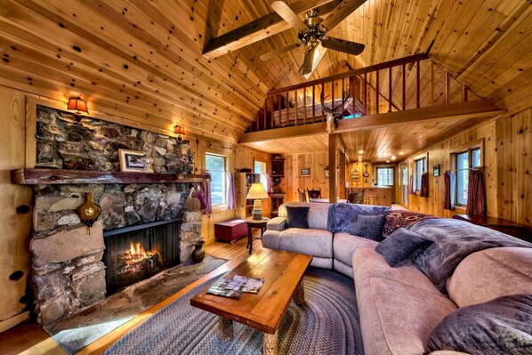 Open concept living room area with large flat screen SmartTV, gas fireplace, vaulted ceilings, dining area, and opens towards large front deck and views of lake.
