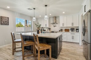 The kitchen features a spacious island with a white marble countertop and a black base, surrounded by wooden chairs with a rustic finish.