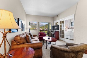 Living area with large mounted flat screen TV, queen size sleeper sofa, wood-burning fireplace, and access to the private balcony.