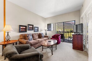 Living area with large mounted flat screen TV, queen size sleeper sofa, wood-burning fireplace, and access to the private balcony.