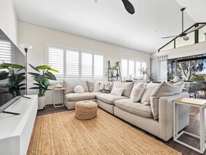 Stretch out and unwind in the spacious main lounge, complete with a comfy sectional, TV, and plantation shutters for coastal privacy and calm.