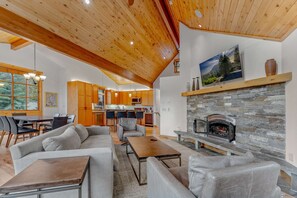 Living Room: Couch, 2 chairs, 55” Smart TV, wood burning fireplace, open layout, forested views, access to upper floor deck