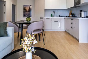 The living area combines elegance and comfort, featuring a sofa with colorful pillows, a dining table with chairs, and pleasant lighting.