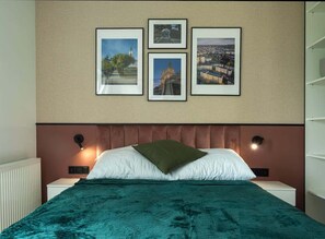 The bed with soft bedding and a green throw creates a calm atmosphere, enhanced by wall art and gentle lighting.