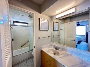The full bathroom with tub and shower combo, and a vanity with cabinet.