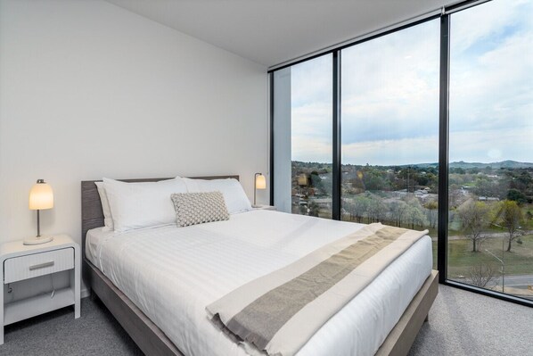 Enjoy a queen-size bed with professionally laundered linens, large windows that fill the room with natural light, and a distant view of the National Arboretum, creating a bright and serene atmosphere.