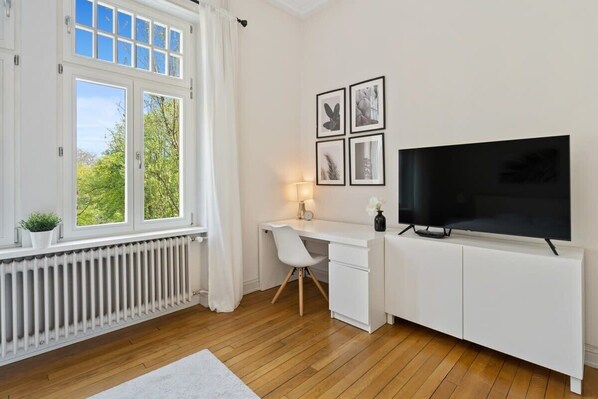 Cozy bedroom with a work desk, flat-screen TV, and large windows for a relaxing and productive stay.