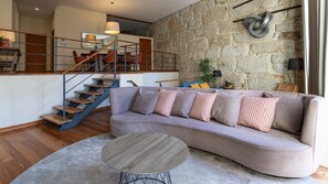 Relax in this beautifully designed living space, complete with a cozy, curved sofa and unique stone wall backdrop. The open-plan layout and elegant staircase lead up to the dining area, creating a seamless flow for entertaining or unwinding. #Airbnb