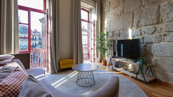 Bask in natural light and stunning city views from the comfort of this inviting living room. Large windows, exposed stone walls, and a stylish, modern decor make this the perfect spot to relax, watch TV, or enjoy a morning coffee.  #LovelyStay