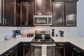 - Modern kitchen with sleek dark cabinetry and appliances for a contemporary feel - Equipped with a microwave, stove, and a coffee maker, providing everything needed for easy meal prep - Clean, bright countertops and backsplash create a polished look
