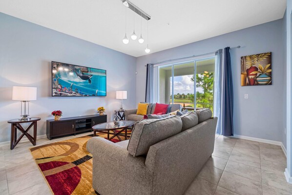 - Comfortable living room featuring a cozy sofa with vibrant accent pillows for a pop of color - Flat-screen TV mounted on the wall, ideal for movie night or relaxing - Natural light streams in through sliding glass doors, leading to a scenic balcony