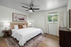 This spacious primary bedroom with a king bed features high-quality linens, blackout curtains for complete privacy, a luxurious en suite bathroom, generous closet, and a soothing design that creates a tranquil and inviting retreat.