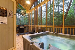 Unwind in the private hot tub surrounded by nature. Your screened-in porch includes cozy seating, a grill, and a mounted TV — perfect for relaxing rain or shine.