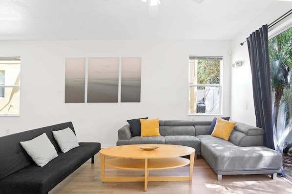 The living room offers a spacious and comfortable area for relaxation. It is equipped with a TV for your entertainment and features a large window, a ceiling fan that provides a pleasant breeze, and a coffee table that adds both functionality and a decorative touch to the space.