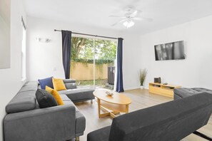 The living room offers a spacious and comfortable area for relaxation. It is equipped with a TV for your entertainment and features a large window, a ceiling fan that provides a pleasant breeze, and a coffee table that adds both functionality and a decorative touch to the space.