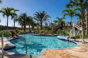 Relax by this inviting pool with a gentle curve, surrounded by lush palm trees and a waterslide, creating a fun tropical oasis for all ages.
