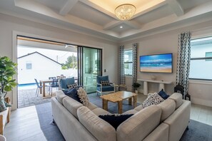 Spacious living room with a 65-inch TV and stunning views through floor-to-ceiling sliding doors, looking out onto the beautiful backyard! | Seaside Sanctuary, Naples, Florida | Voyax Luxury Vacation Rentals