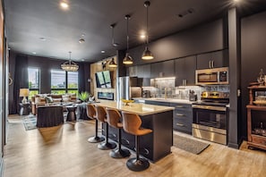 Modern and stylish open-concept kitchen and living area. The kitchen features dark cabinets, a sleek white countertop, and contemporary bar stools.