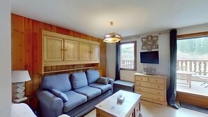 This inviting living area features a comfortable sofa, a coffee table, and a flat-screen TV. Sliding doors lead to a private terrace with a view of the surrounding mountain landscape.  The warm wood paneling on the walls adds a touch of rustic charm to th