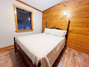 Rustic bedroom with a cozy bed, wooden walls, and a warm ambiance.