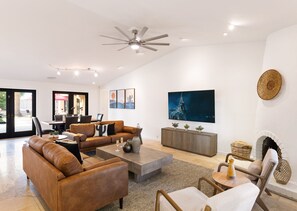 Bright open floor living space featuring a smart flat-screen TV, designer furnishings, and access to the outdoor patio leading to the attached casita and pool/spa area. Fireplace not functional.