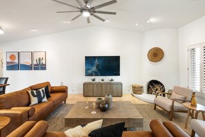 Bright open floor living space featuring a smart flat-screen TV, designer furnishings, and access to the outdoor patio leading to the attached casita and pool/spa area. Fireplace not functional.