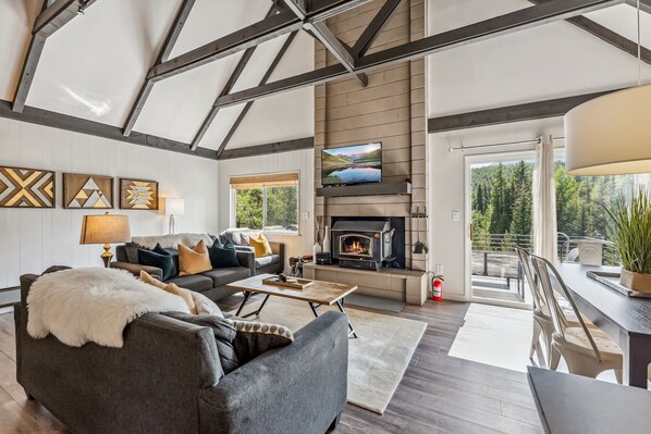 Living Room: 2 couches, chair, 43” TV, wood-burning fireplace, board game & books, deck access, mountain, tree, & river views