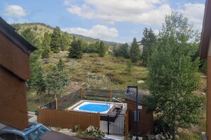 View of a small fenced pool surrounded by trees, with mountains in the background under a partly cloudy sky.