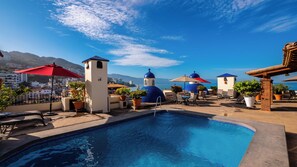 Rooftop pool area with plenty of loungers and tables and chairs with umbrellas.