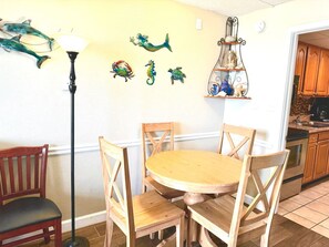 The oceanfront dining room features a cozy table with four chairs, perfect for enjoying meals while overlooking the stunning ocean views. The space is decorated with a beach theme and coastal accents.