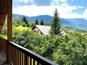 Enjoy stunning mountain views from the private terrace of one of the bedrooms, accessible via a wooden deck. The terrace offers a peaceful escape surrounded by lush greenery and a tall pine tree, providing a sense of privacy and tranquility.