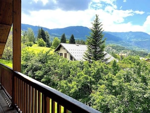 Enjoy stunning mountain views from the private terrace of one of the bedrooms, accessible via a wooden deck. The terrace offers a peaceful escape surrounded by lush greenery and a tall pine tree, providing a sense of privacy and tranquility.