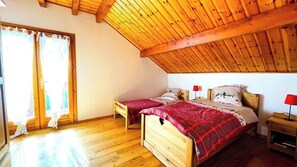 This charming bedroom features a wooden beamed ceiling and large windows that offer stunning views of the surrounding mountains. Two twin beds are tastefully appointed with red and white plaid bedding, ensuring a comfortable and cozy sleep. The wooden flo