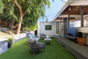 Discover our serene seating area at the rear of our mid-century modern house, nestled in abundant shade throughout the day. Enjoy a tranquil setting with a TV and Zen garden, ideal for relaxation. You'll find seating for four at the table, perfect for streaming Netflix or your favorite shows on any service of your choice